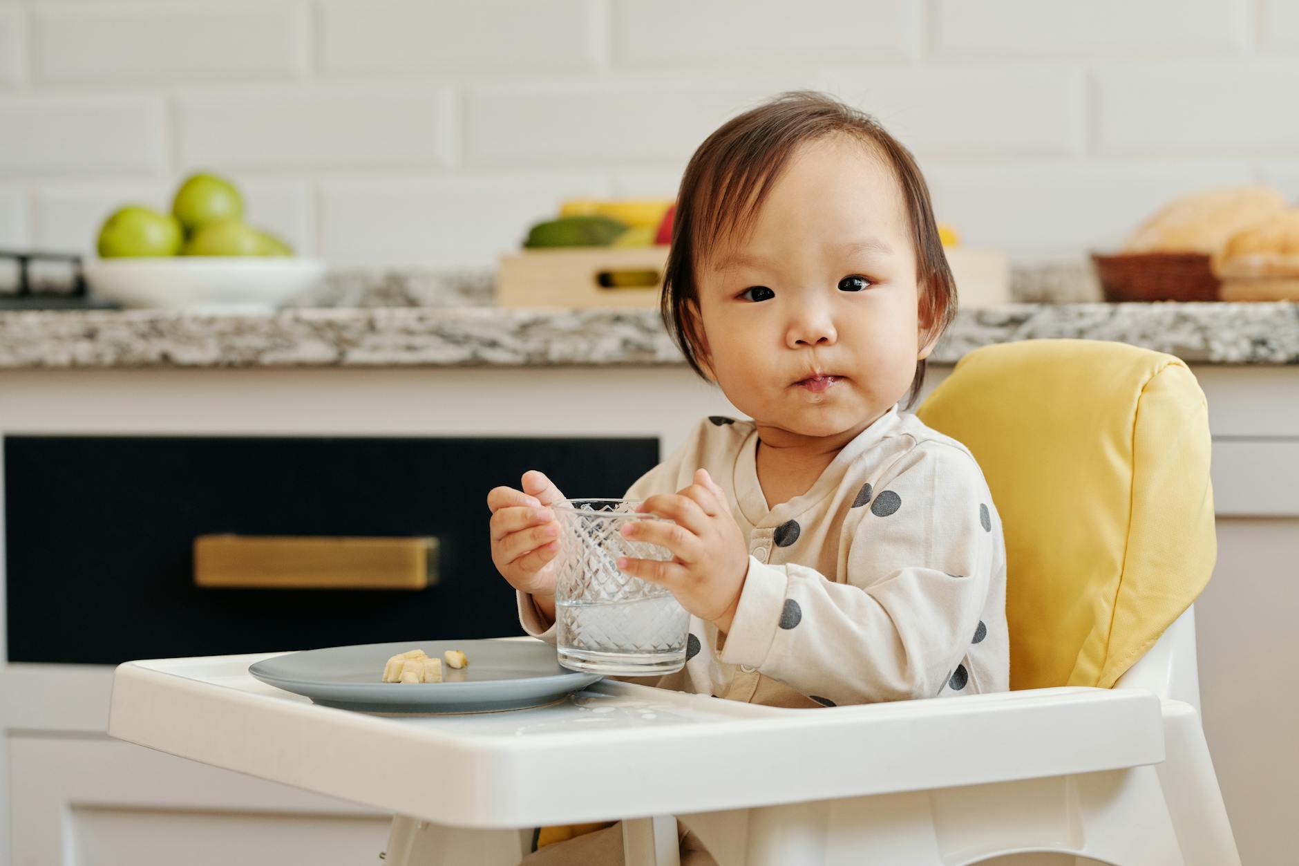 a toddler eating and drinking sitting on high chair